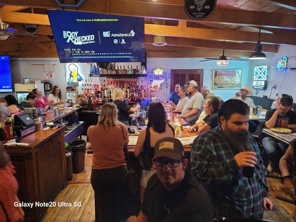 Crowded bar interior with patrons at the counter and neon signs overhead