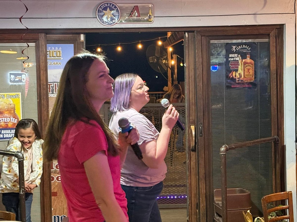 Two women singing karaoke together at a bar, holding microphones