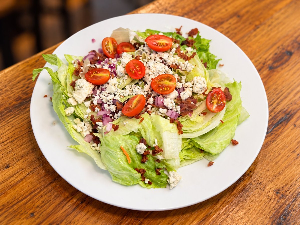 Fresh salad on white plate with lettuce, tomatoes, feta cheese, and red onions on wooden table