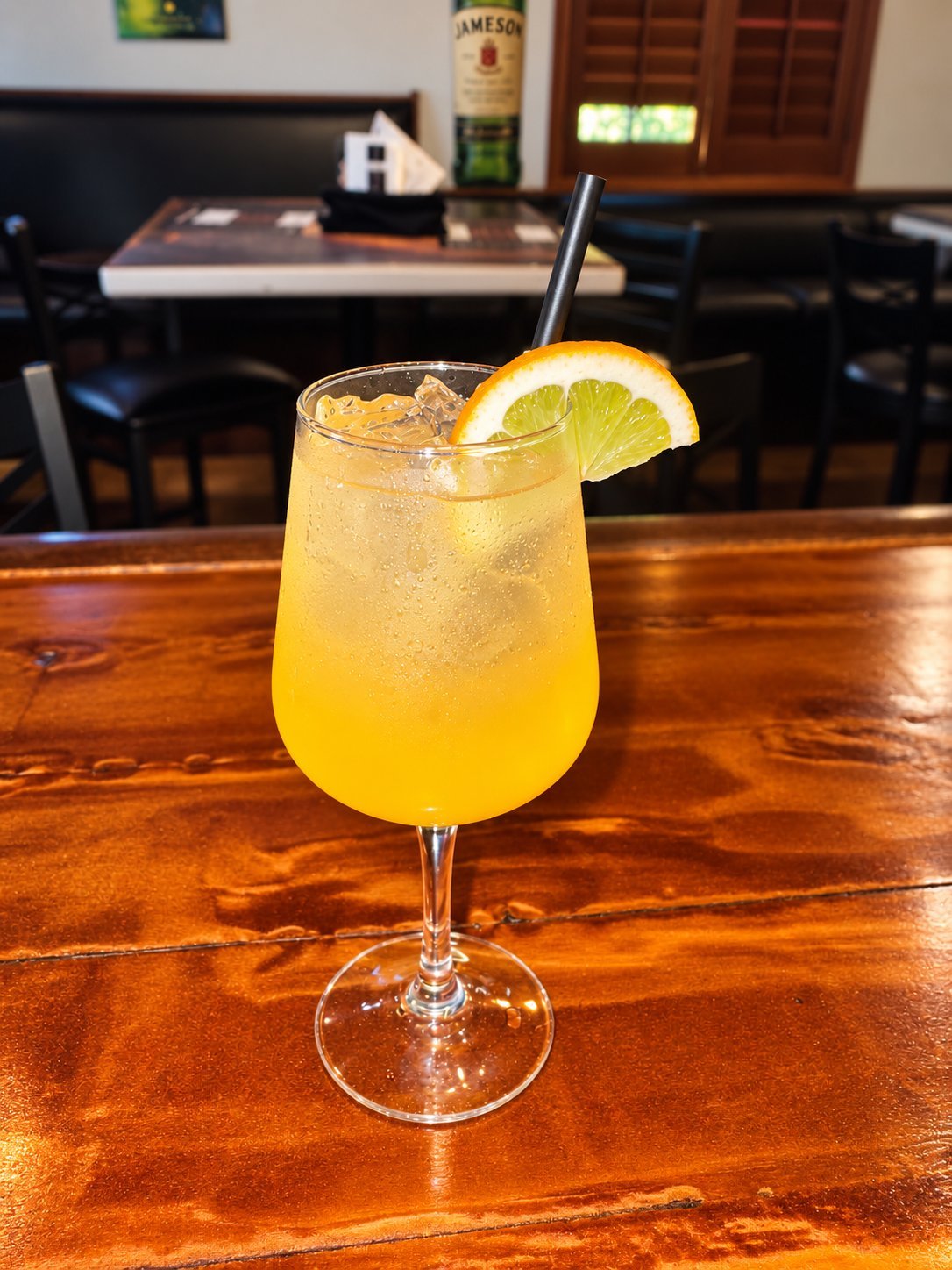 Yellow cocktail with ice and a lime slice on a wooden bar counter, with a Jameson bottle visible in the background