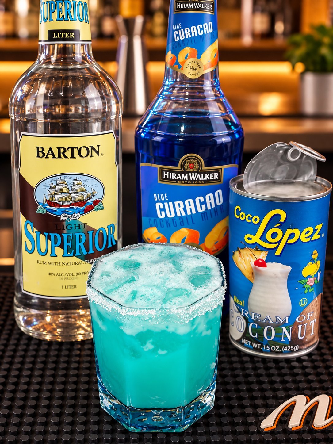 Turquoise cocktail with ice surrounded by Barton rum, Hiram Walker Blue Curacao, and Coco Lopez coconut cream bottles