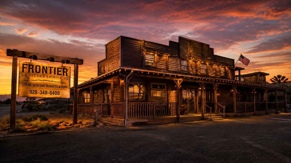 Illuminated Old West-style wooden buildings at dusk with a Frontier sign and dramatic orange sunset sky